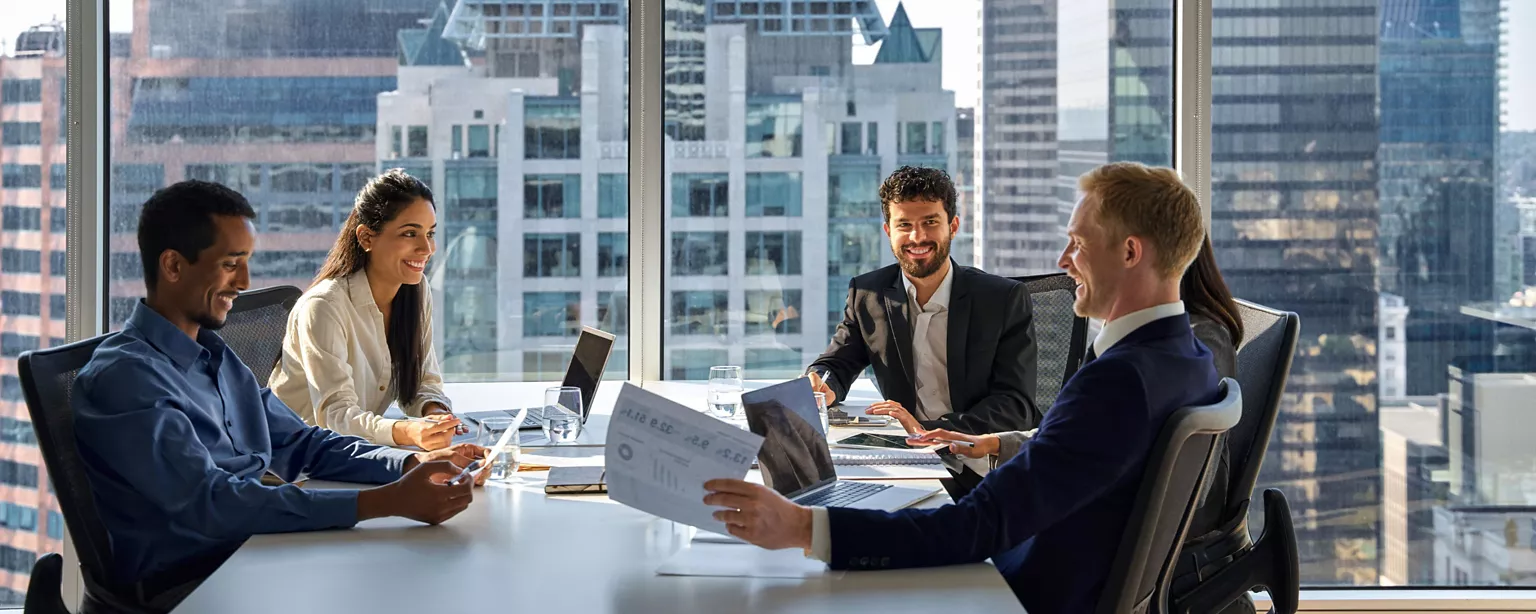 A group of professionals engaged in a productive meeting in a windowed office with a city skyline in the background.